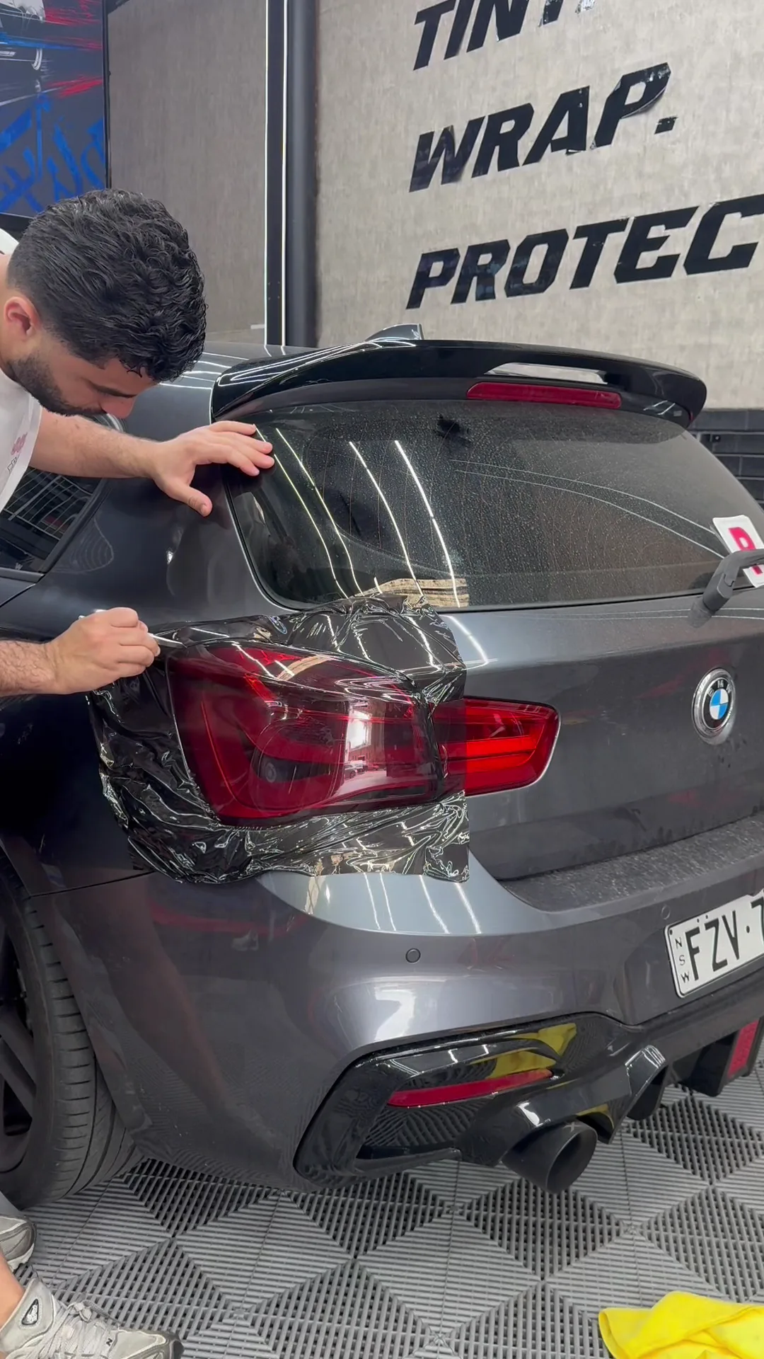 A technician fitting film over the left rear light of a grey BMW at Wally’s
